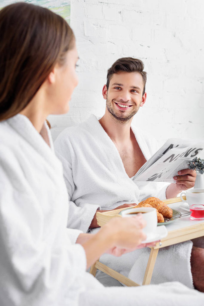 young family in bathrobes having breakfast and reading newspaper in bed - Photo, Image