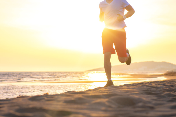 Вид з низької секції людини, що біжить на пляжі проти заходу сонця
 - Фото, зображення