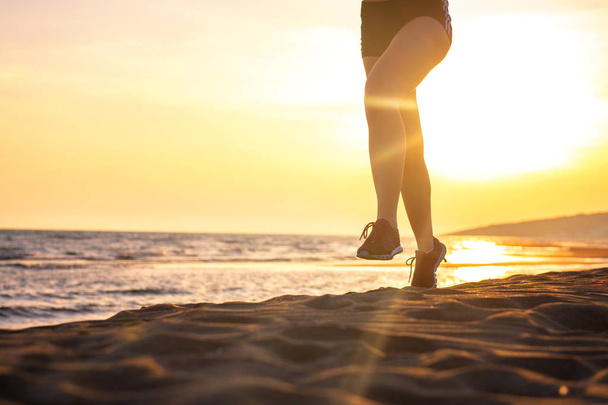 Низкий вид на женщину, бегущую против восходящего неба на пляже
 - Фото, изображение
