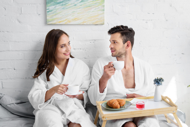 young couple in bathrobes having breakfast in bed in morning - Fotografie, Obrázek