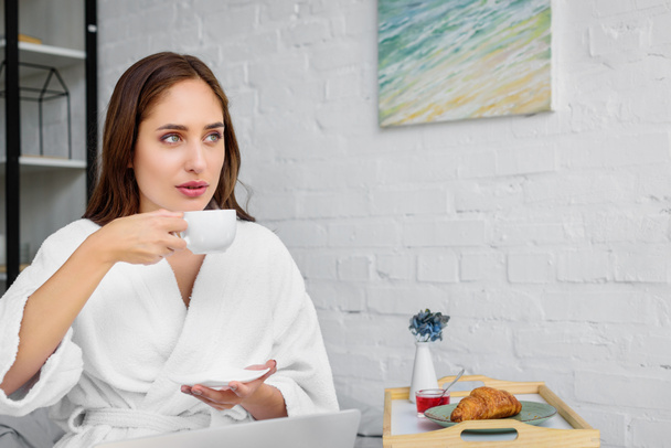 beautiful woman in white bathrobe drinking coffee for breakfast in bedroom  - 写真・画像