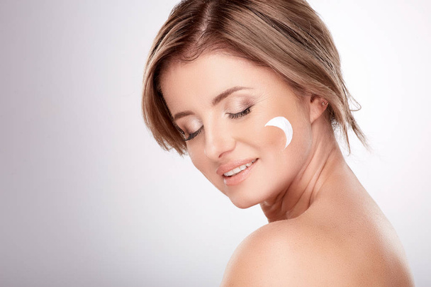 pretty smiling young woman using facial cream at grey background, beauty photo, skin care, spa concept - Photo, Image