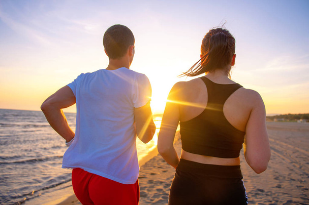 Meio comprimento visão traseira de casal encantador jogging juntos na praia
 - Foto, Imagem
