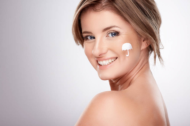 vrij lachende jonge vrouw met naakte schouders met behulp van gezichtscrème, schoonheid foto concept, huid en rimpels behandeling, UV-bescherming - Foto, afbeelding