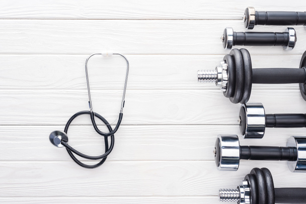 top view of various dumbbells and stethoscope on white wooden surface - Foto, immagini