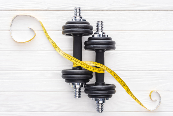 top view of dumbbells and yellow measuring tape on wooden surface - Photo, Image