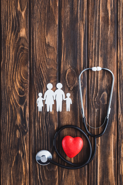 top view of white figures of family holding hands, red heart symbol and stethoscope on wooden table - Photo, Image