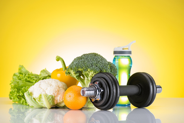 dumbbell, bottle of water and fresh orange and vegetables on yellow  - Photo, Image