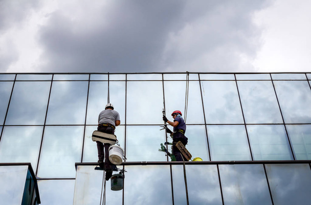 Промислові альпіністи застосовують силіконову гумову розв'язку серед скляного фасаду будівлі
. - Фото, зображення