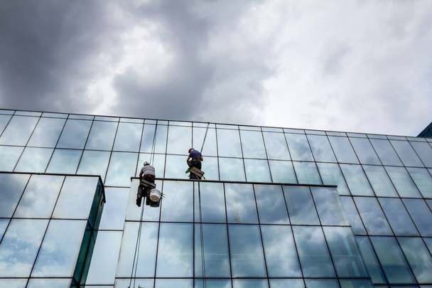 Gli arrampicatori industriali stanno applicando silicone alla giuntura di gomma tra la facciata in vetro dell'edificio
. - Foto, immagini
