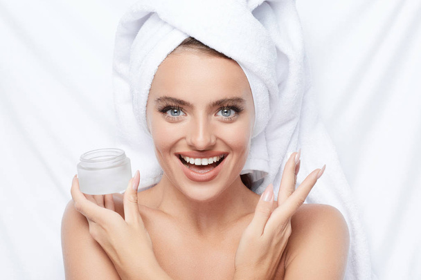 muito sorrindo jovem mulher usando creme no fundo branco, toalha na cabeça, foto de beleza, cuidados com a pele, conceito de spa
 - Foto, Imagem