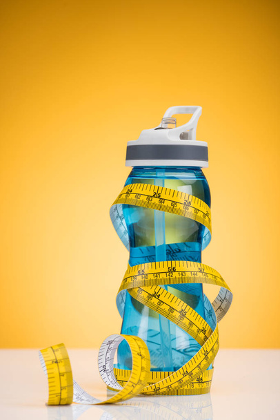 Close-up beeld van sportfles met water en het meetlint op geel - Foto, afbeelding