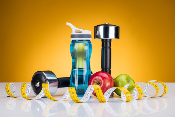 vista de cerca de pesas, cinta métrica, botella de agua y manzanas en amarillo
 - Foto, Imagen