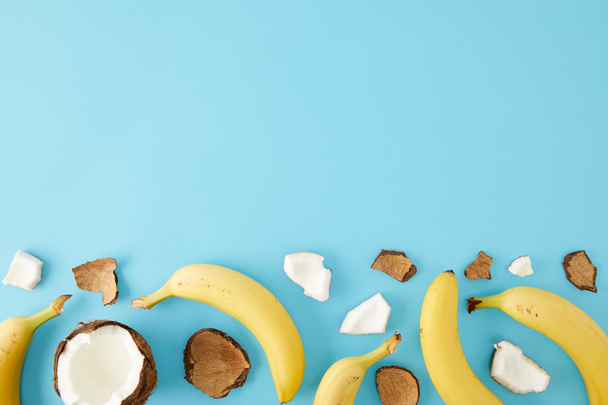 top view of arranged coconut pieces and bananas isolated on blue - Fotografie, Obrázek