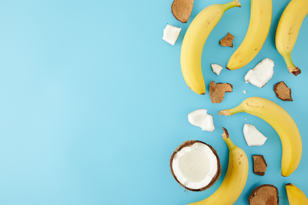 bovenaanzicht van gearrangeerde kokosnoot stukken en bananen geïsoleerd op blauw - Foto, afbeelding