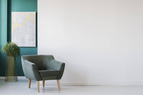 Minimalist living room interior with empty, white wall, green armchair, plant and painting - 写真・画像