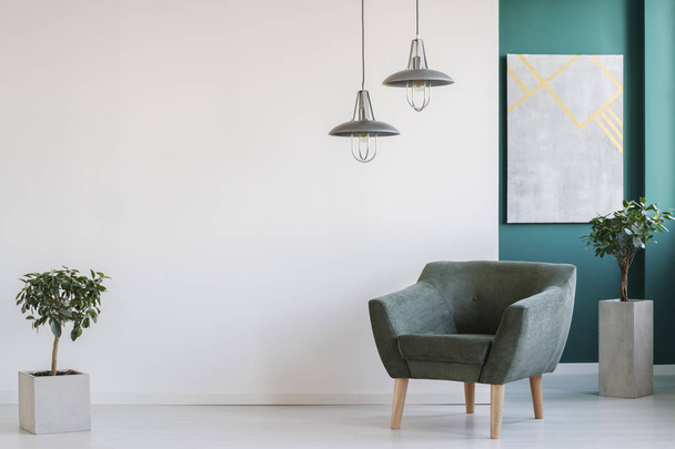 Concrete planters, industrial chandeliers and a dark, modern armchair in a minimalist living room interior - Foto, afbeelding