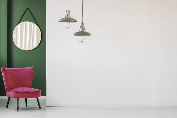 Minimalist living room interior with white, empty wall, comfortable retro chair and a round hanging mirror in green corner - Foto, Bild