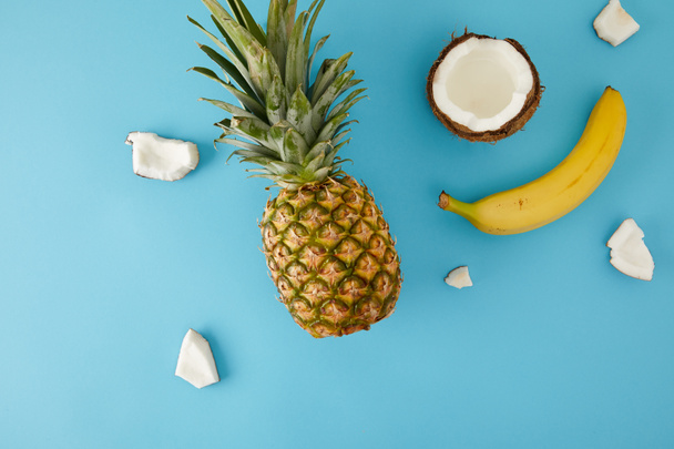 flache Lage mit reifen Ananas-, Bananen- und Kokosstücken isoliert auf blau - Foto, Bild