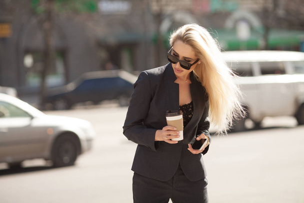 Cheerful female manager getting to work by foot drinking morning coffee to go while walking street, successful businesswoman in elegant wear enjoying sunny weather - Foto, Bild