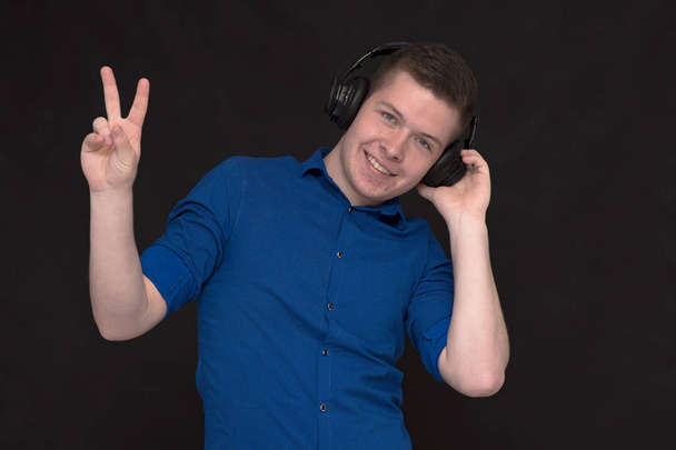 I like listening to music. Portrait of a young handsome man on a black background with headphones listening to music. He stands right in front of the camera smiling and looks happy - Valokuva, kuva