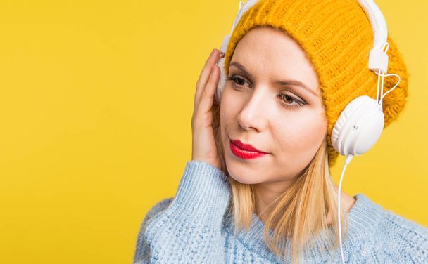Portrait of a young beautiful woman with headphones in studio on a yellow background. - Photo, image