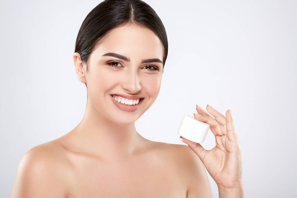 jeune femme naturelle souriante tenant la crème sur la peau sur fond gris
 - Photo, image
