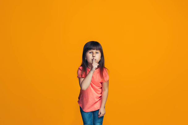 The young teen girl whispering a secret behind her hand over orange background - Fotoğraf, Görsel