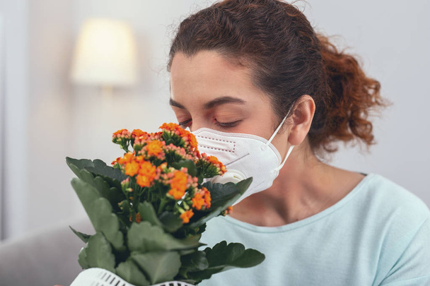 Young girl smelling a potted flower while wearing a respiratory mask - Foto, afbeelding