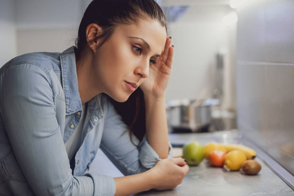 Sad girl leaning on a kitchen counter top and thinking - Fotografie, Obrázek