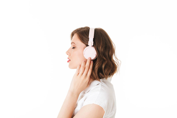 Portrait of beautiful lady listening music in headphones while dremily closing her eyes on white background isolated - Photo, image