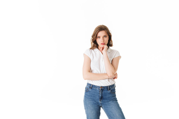Porträt einer jungen Frau, die in T-Shirt und Jeans steht und nachdenklich in die Kamera auf weißem Hintergrund blickt - Foto, Bild