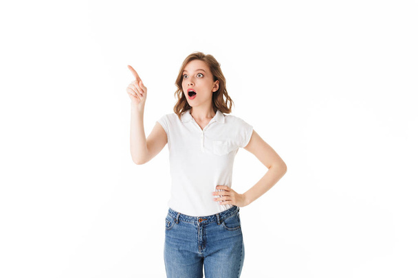 Portrait of young shocked lady standing in t shirt and jeans and amazedly looking aside on white background isolated - Photo, image