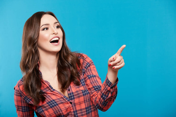 cute young woman pointing at something against blue background - Photo, image