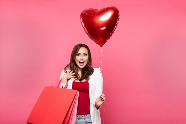 mujer feliz joven con bolsas de compras y globo en forma de corazón posando sobre fondo rosa, compras y concepto de descuento
 - Foto, imagen