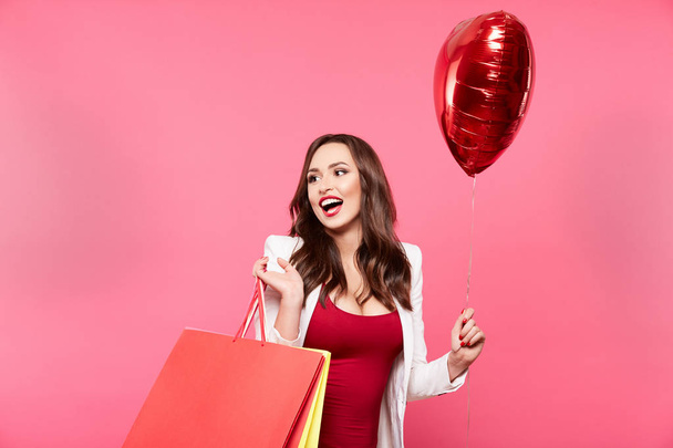Alışveriş torbaları ve kalp şekli balon pembe arka plan, alışveriş ve indirim kavramı karşı poz olan mutlu kadın - Fotoğraf, Görsel