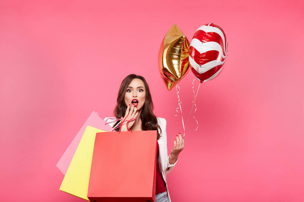 young happy woman with shopping bags and balloons posing against pink background, shopping and discount concept - Foto, imagen