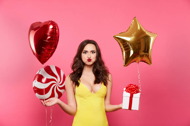 Gelukkig jonge vrouw met ballonnen en de doos van de gift die zich voordeed op roze achtergrond - Foto, afbeelding