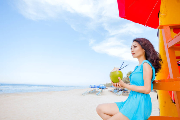 Young beautiful asian woman is drinking coconut juice on the tropical sea beach - Fotoğraf, Görsel