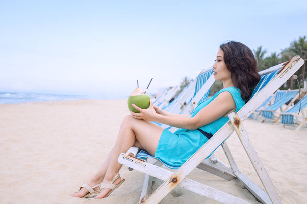 Young beautiful asian woman is drinking coconut juice on the tropical sea beach - Φωτογραφία, εικόνα