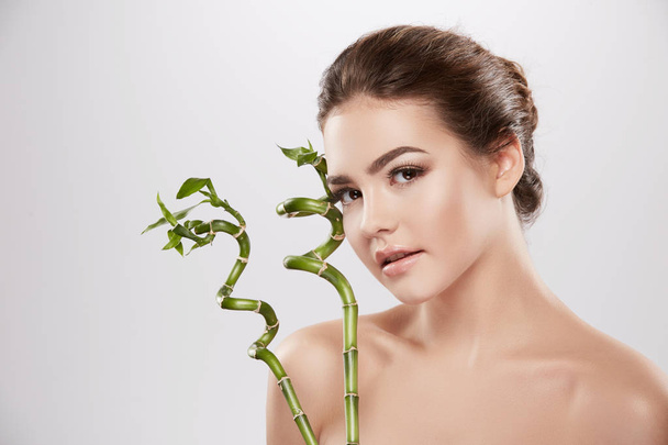 természetes és gyönyörű fiatal nő pózol zöld bambusz növények a szürke háttér, skin care koncepciót, hidratált bőr - Fotó, kép
