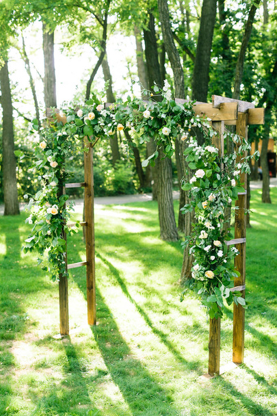 morning, celebration, decoration concept. wedding arch in the form of hoops for ceremony decorated with white roses and carnationa standing out in tender lights of spring rising sun - Photo, Image
