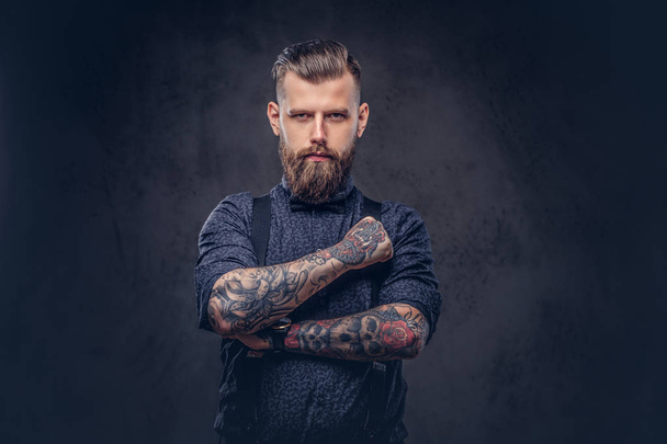 Portrait of a handsome old-fashioned hipster in a blue shirt and suspenders, standing with crossed arms in a studio. - Photo, Image
