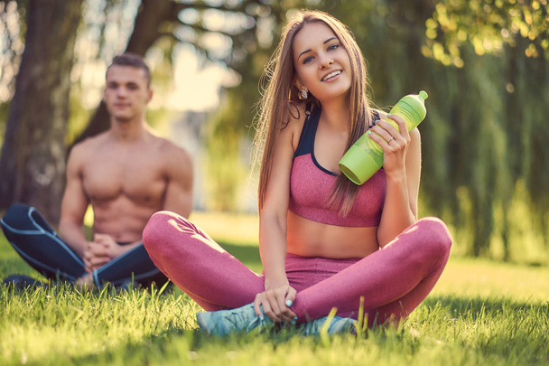 Egészséges életmód fogalma. Boldog fiatal fitness házaspár ült a lótusz póz a zöld fű. - Fotó, kép