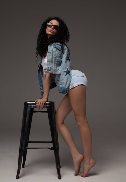 Sexy attractive brunette woman posing in fashionable jeans in studio. Fashion model posing. Long curly hair. - Φωτογραφία, εικόνα
