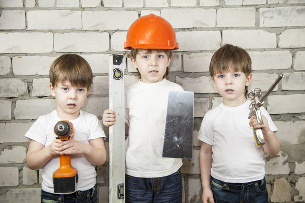 Le concept de construction, ("ensemble, nous sommes la force") ; garçon dans un casque d'ouvrier de la construction avec des outils pour mastic, sur un fond de mur de briques blanches avec des frères jumeaux
 - Photo, image
