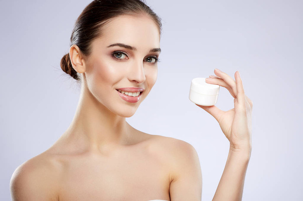 young smiling natural woman applying cream on skin against grey background - Foto, Imagen