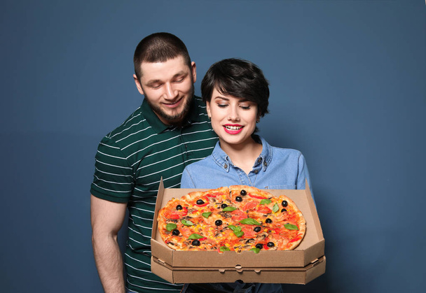 Attractive young couple with delicious pizza on color background - Фото, изображение