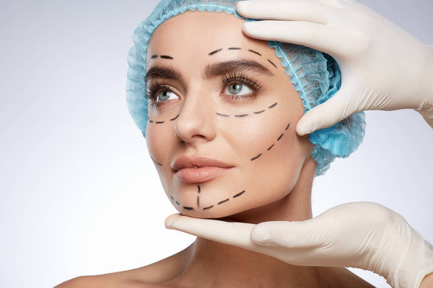 портрет привлекательной женщины, концепция пластической хирургии. Модель с проколами на лице, руки в перчатках касаются ее лица
  - Фото, изображение
