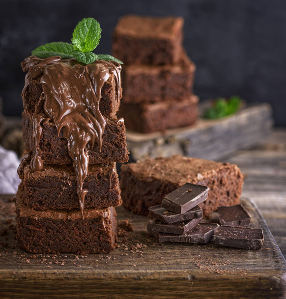 Vierkante stukjes chocolade cake zijn bedekt met een dikke laag chocolade, close-up - Foto, afbeelding